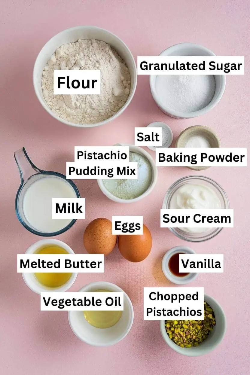 Ingredients for pistachio muffins including flour, granulated sugar, salt, baking powder, pistachio pudding mix, milk, sour cream, two eggs, vanilla, melted butter, oil, and chopped pistachios.