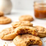 A couple of apple butter cookies on a white marble surface, and a glass jar filled with apple butter behind the cookies.