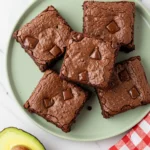 Avocado brownies on a light green plate with half avocado and a napkin next to the plate.