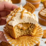 A hand holding a Biscoff cupcake with a bite taken out of it revealing the Biscoff butter filling inside.