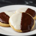 Black and white cookies are placed on a white plate against a dark marble surface.