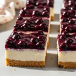 Delicious blueberry cheesecake bars on a gray surface.