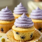 Blueberry Cupcakes on a light-yellow surface and a few Marguerite flowers scattered around.