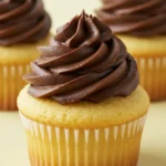 Three Boston cream cupcakes placed on a light-yellow surface.