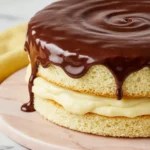 Boston cream pie on a light pink marble plate against a white marble surface.