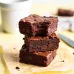 Stack of Two Brown Butter Brownies arranged on parchment paper against a light yellow background.