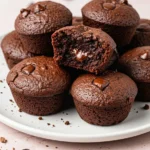 Brownie bites on a white plate against a light pink surface.