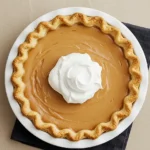 Butterscotch pie in a white pie dish topped with whipped cream.
