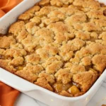 Caramel apple dump cake in a white pan and an orange napkin beneath it.