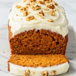 Carrot Cake Loaf with cream cheese frosting on a white rectangular marble plate against a white marble surface.