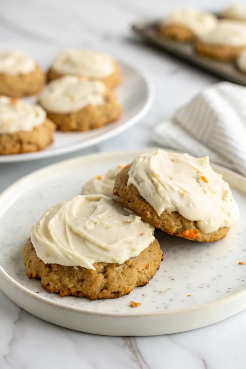Carrot cake cookies with cream cheese on a white plate against a marble surface.
