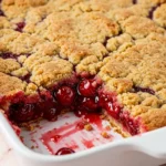 Cherry dump cake on a white pan with a slice missing.