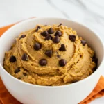 Chickpea cookie dough in a white bowl and an orange napkin under the bowl.