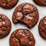 Chocolate brownie cookies on a white marble plate against a light pink surface.