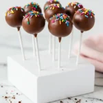 Chocolate cake pops on a styrofoam block against a white marble surface.