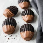 Chocolate Madeleines, half-dipped in milk chocolate placed on a parchment paper.