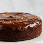 Chocolate orange cake placed on a white marble plate against a white white marble surface.