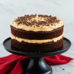 Chocolate peanut butter cake on a black cake stand against a white marble surface.