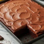 Chocolate sheet cake with a slice missing on a black baking sheet against a white marble surface.
