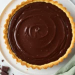 Chocolate tart on a large white plate and a light green napkin beside it.