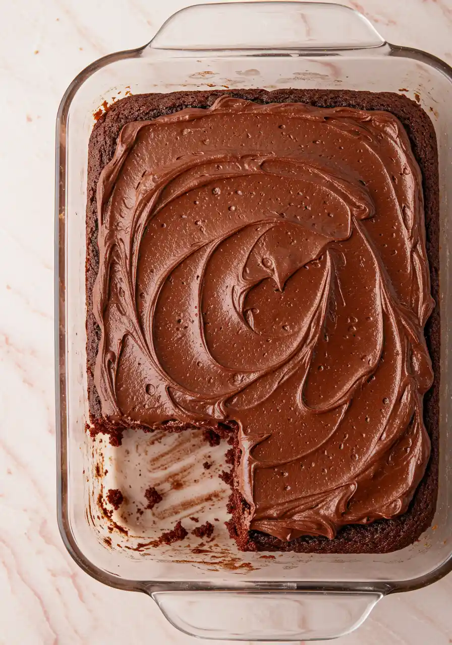 Chocolate zucchini cake on a glass baking dish against a light pink surface.
