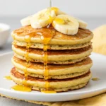 A stack of coconut flour pancakes topped with banana slices and honey.