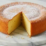 Condensed milk cake placed on a white marble plate with a slice missing.
