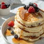 Cottage Cheese Pancakes on a white plate drizzled with honey and topped with fresh berries.