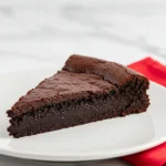 A slice of flourless chocolate cake is placed on a white plate and a red napkin next to it.