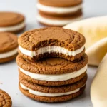 A stack of gingerbread sandwich cookies and the top one has a bite missing.