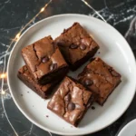 Greek yogurt brownies on a white plate against a dark marble surface and LED strings are glowing on the surface.