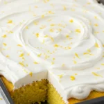 Lemon poke cake on a black baking dish placed on a white marble surface.