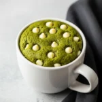 Matcha mug cake on a light gray surface and a black napkin beside it.