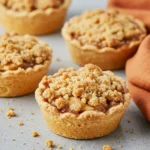 Mini apple pies on a gray surface and an orange napkin around.