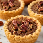 Mini pecan pies on a white marble surface.