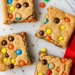 M&M cookie bars on a white marble surface and a red napkin beside them.