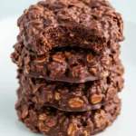 Stack of no-bake cookies placed on a white plate, with the top cookie having a bite taken out of it.