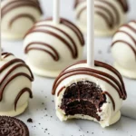 Oreo cake pops on a white marble surface and one pop has a bite taken out of it.