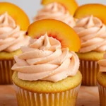 Peach cupcakes placed on a light orange surface.