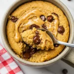 Peanut butter mug cake placed on a white marble surface with a spoon on it.