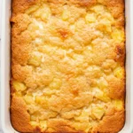 Pineapple dump cake on a white pan against a white marble surface.
