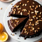 Prolific oven chocolate orange almond cake recipe topped with sliced almonds and a slice taken out of it.