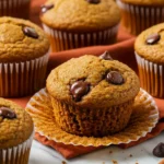 Pumpkin chocolate chip muffins above a dark orange napkin and some chocolate chips around.