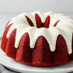 Red velvet bundt cake on a white plate drizzled with a cream cheese glaze.
