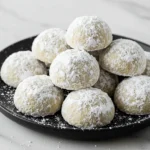 Snowball cookies on a black plate.