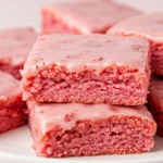Strawberry brownies on a white plate against a light pink surface.