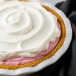 Strawberry cream pie topped with whipped cream in a white dish.