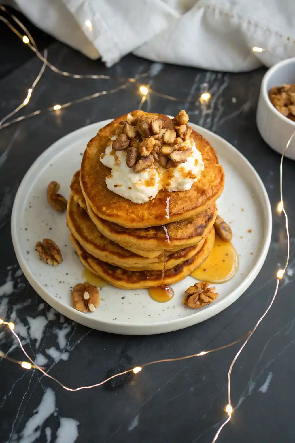 Sweet potato pancakes on a white plate against a dark marble surface with LED string lights around the plate.