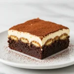 A slice of tiramisu Brownies on a white plate against a white marble surface.