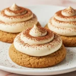 Three tiramisu cookies on a white plate against a light pink marble surface.